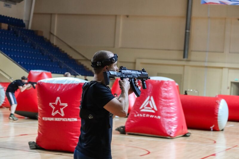Боец LASERWAR прицеливается из-за красного укрытия.